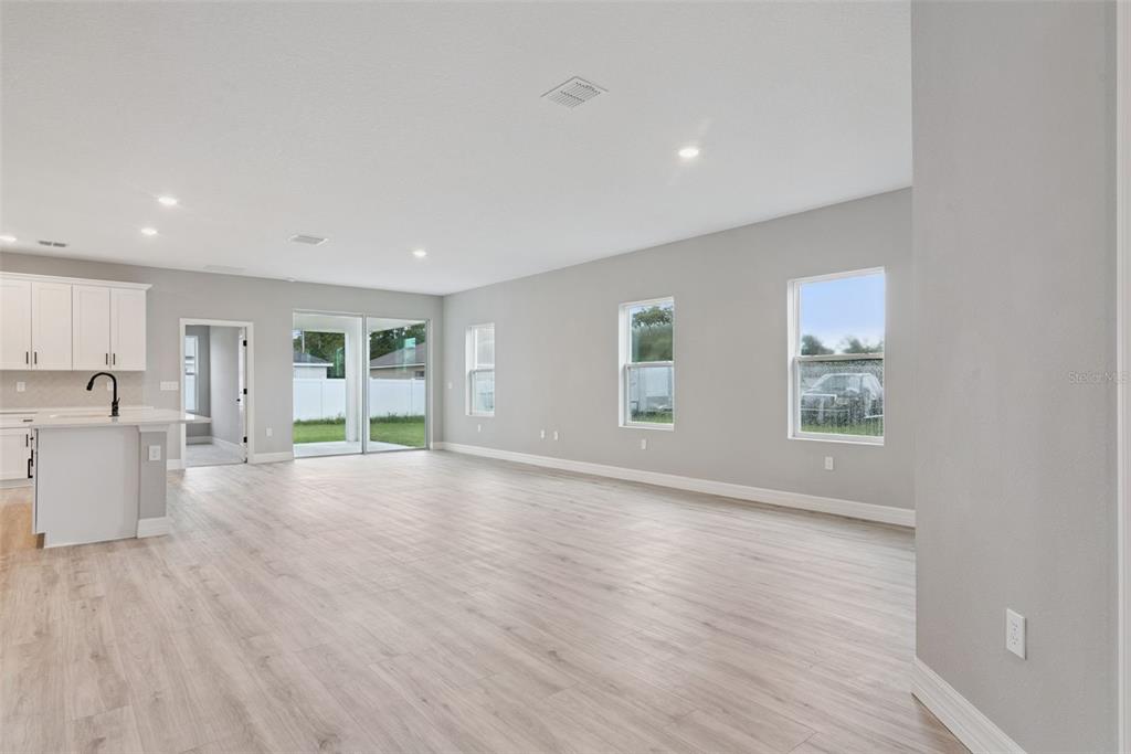 An open-concept living area features light wood-look flooring, gray walls, and an adjacent kitchen — 489 MARION OAKS TRAIL, OCALA, FL