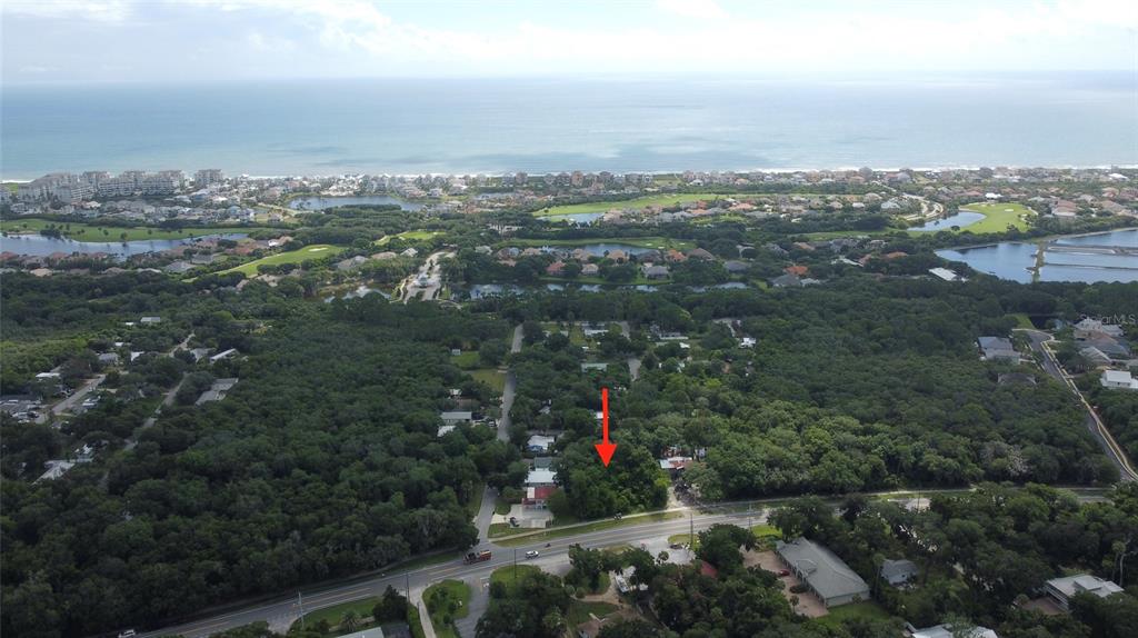 An aerial view shows a wooded lot marked by a red arrow near a road — 5049 N OCEAN SHORE BOULEVARD, PALM COAST, FL