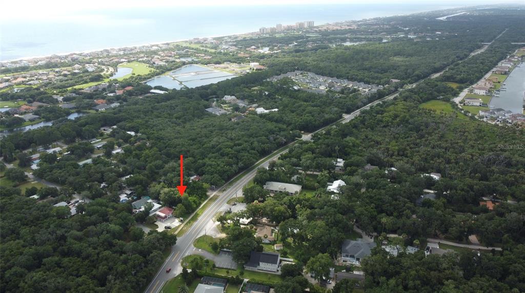 An aerial view shows a house with a red arrow pointing toward its wooded lot — 5049 N OCEAN SHORE BOULEVARD, PALM COAST, FL