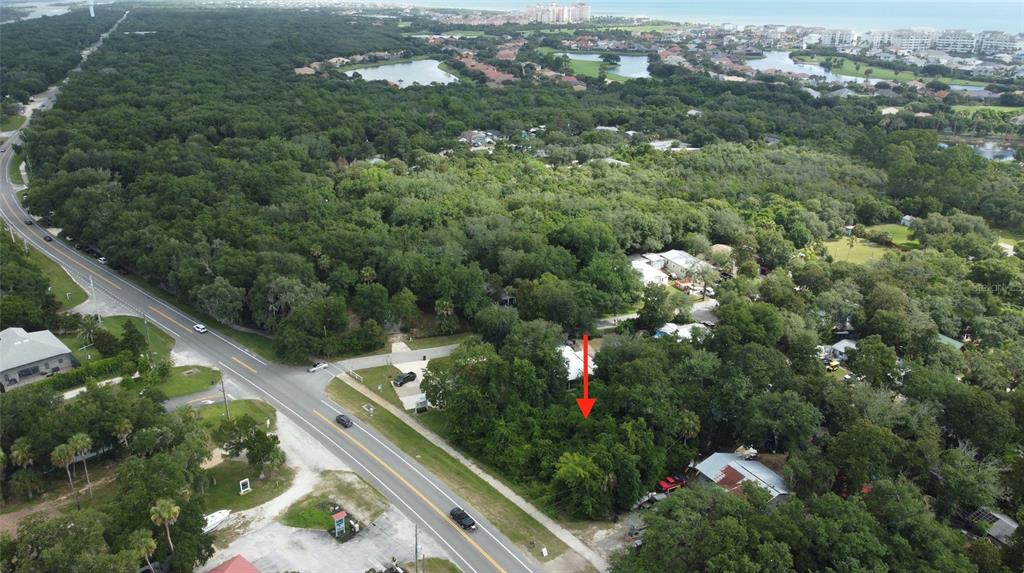 An aerial view shows a wooded lot marked by a red arrow near a road — 5049 N OCEAN SHORE BOULEVARD, PALM COAST, FL