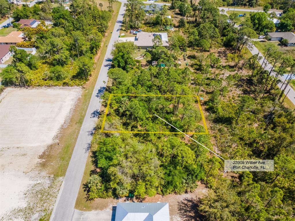 An aerial view shows a rectangular wooded lot outlined in yellow along a paved road — 23309 WILBER AVENUE, PUNTA GORDA, FL