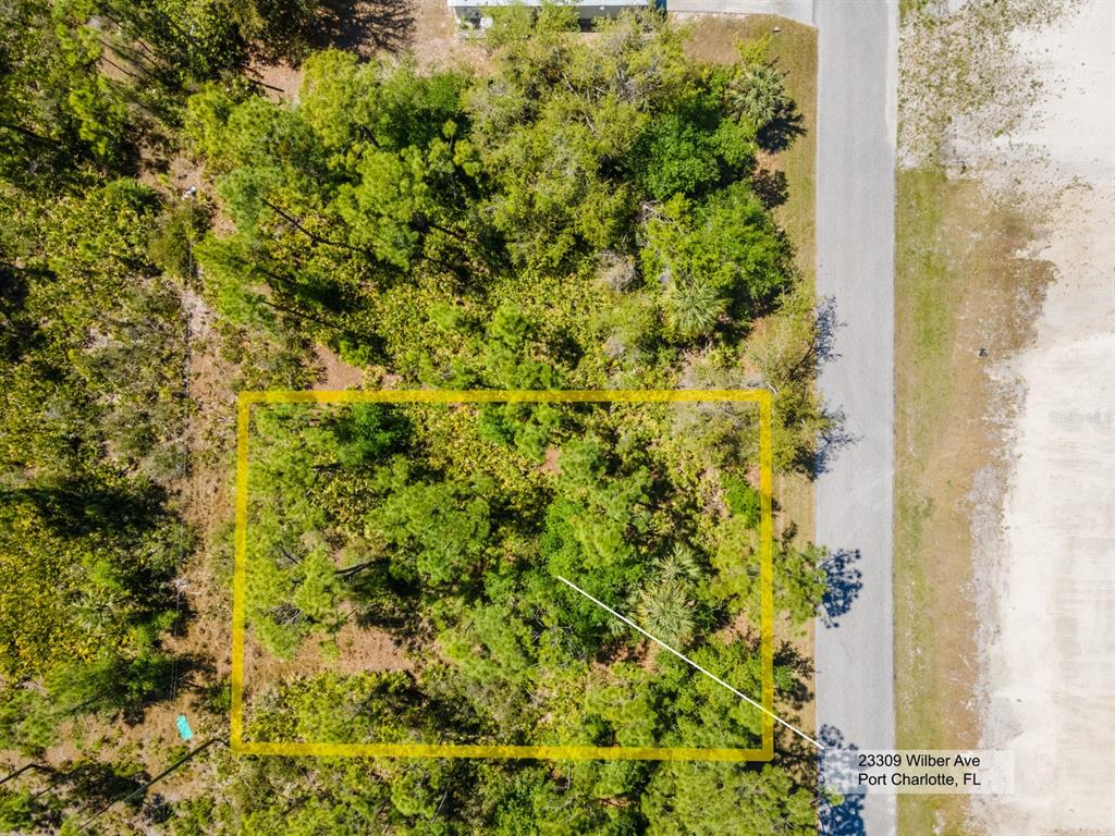 An aerial view shows a rectangular, wooded vacant lot outlined in yellow next to a road — 23309 WILBER AVENUE, PUNTA GORDA, FL