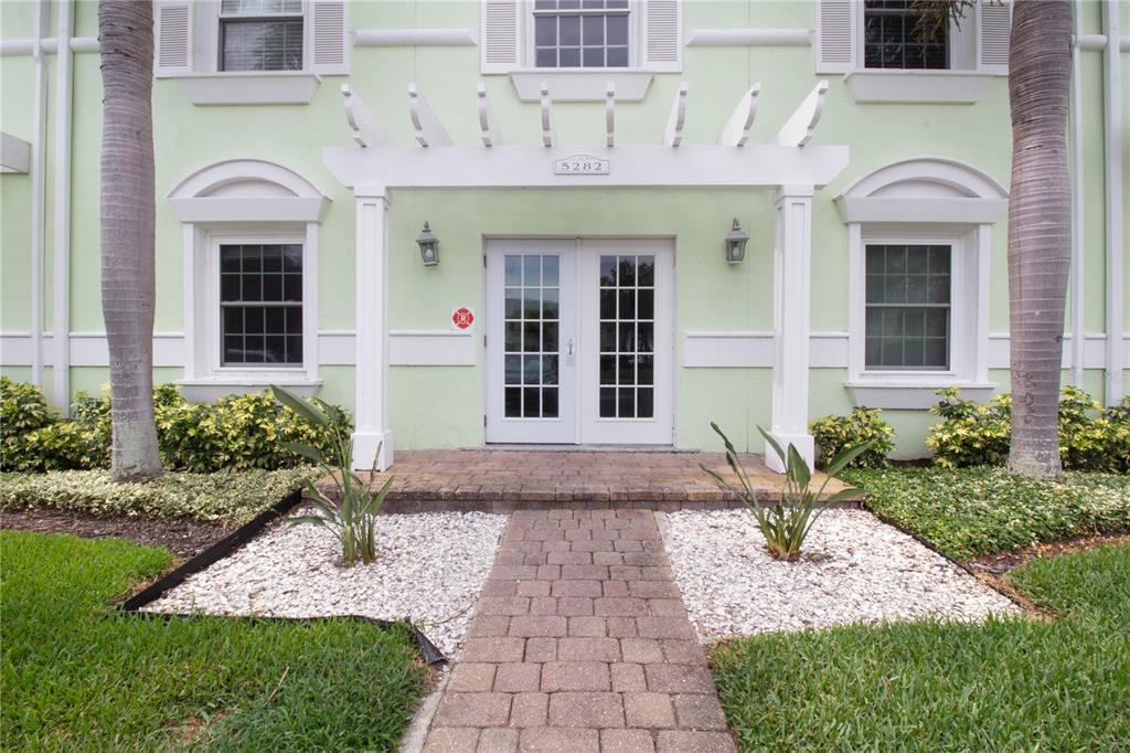 A light green building exterior features a white pergola entrance and a brick walkway — 5282 BEACH DRIVE SE APT D, ST PETERSBURG, FL
