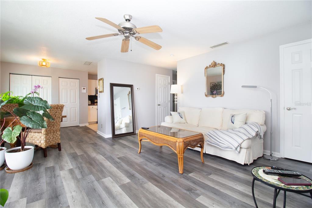 A living room features gray wood-look flooring, a white sofa, and a wicker coffee table — 5282 BEACH DRIVE SE APT D, ST PETERSBURG, FL