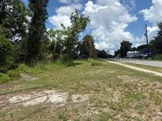 A vacant, grassy lot sits beside a paved road under a cloudy blue sky — 801 S DIXIE AVENUE UNIT A, FRUITLAND PARK, FL