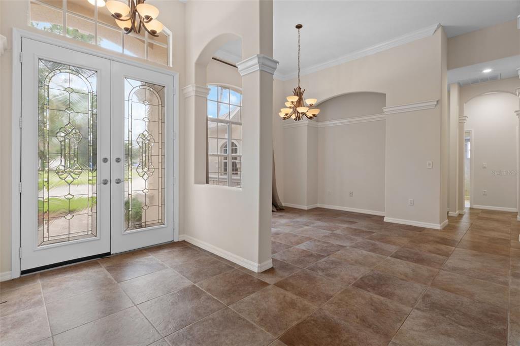 An entryway with tiled floors, double glass-paneled doors, and an adjacent dining area with chandelier — 5141 CHAMPIONSHIP CUP LANE, SPRING HILL, FL
