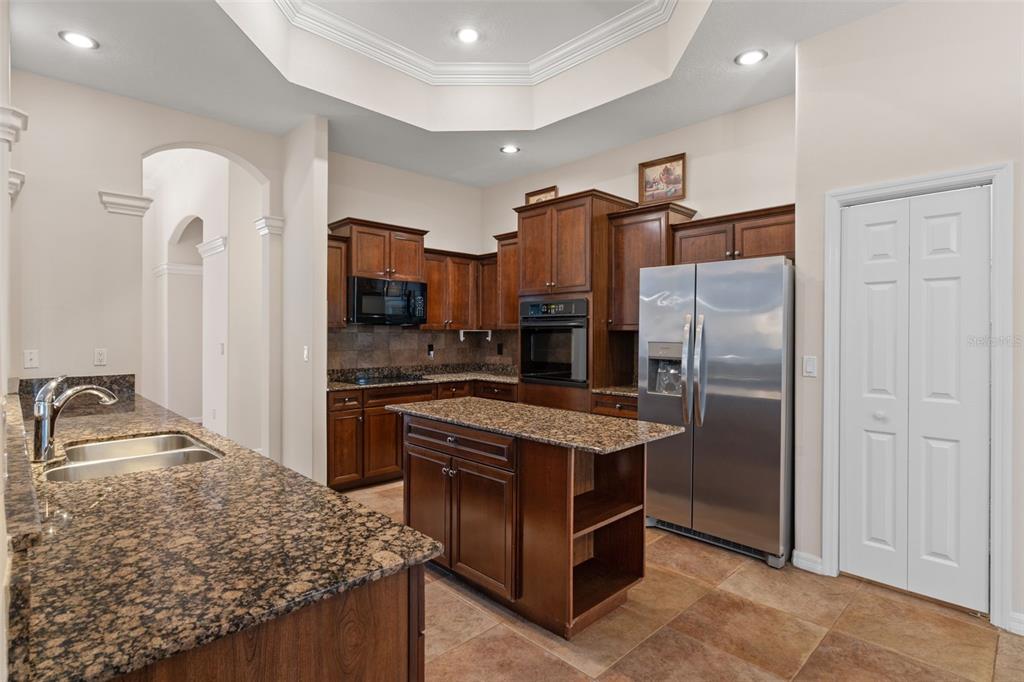 A kitchen with dark wood cabinets, granite countertops, stainless steel appliances, and a center island — 5141 CHAMPIONSHIP CUP LANE, SPRING HILL, FL