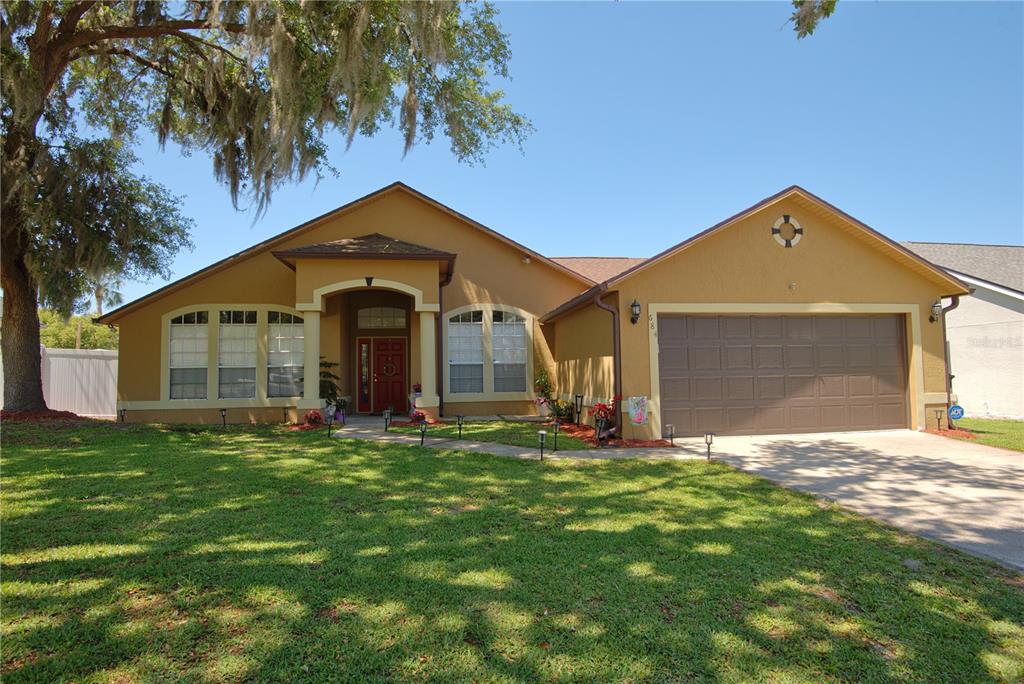 A single-story house with a tan stucco exterior, a two-car garage, and a large tree — 684 YORKSHIRE DRIVE, OVIEDO, FL