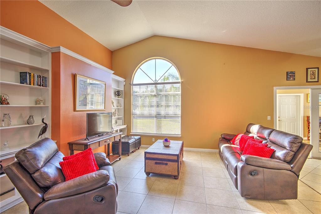 A living room with tile floors, vaulted ceilings, built-in shelving, and brown leather furniture — 684 YORKSHIRE DRIVE, OVIEDO, FL