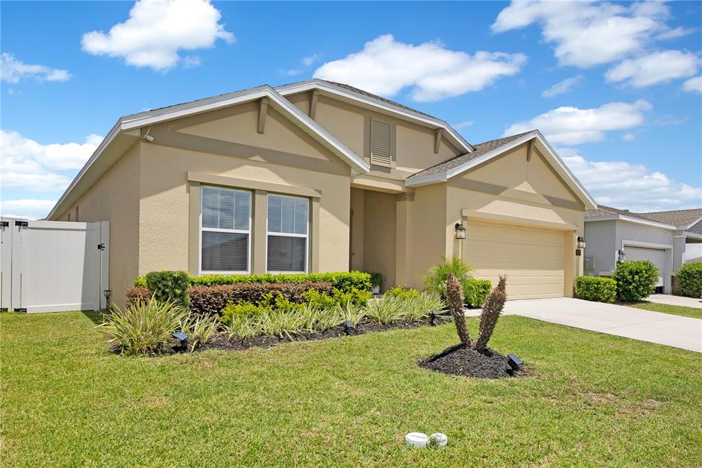 A tan single-story house with a two-car garage and a white vinyl privacy fence — 815 KAPI DRIVE, GROVELAND, FL