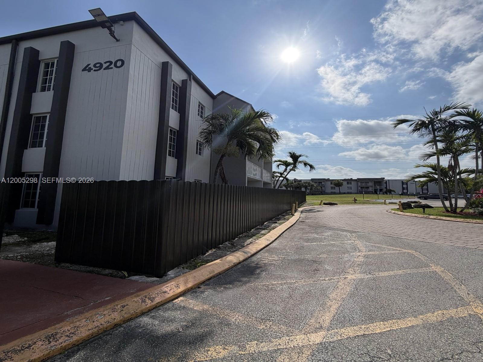 An exterior view of a multi-story apartment building with a dark fence and palm trees — 4920 NW 79th Ave # 313, Doral FL 33166, DORAL, FL
