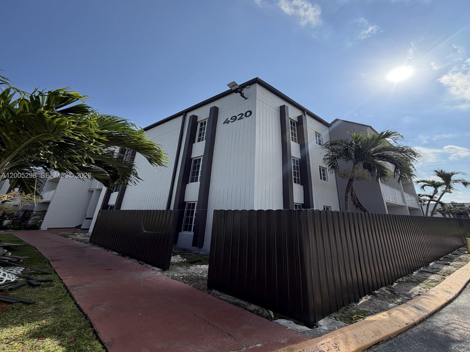 A three-story apartment building features white vertical siding, dark trim, and a surrounding metal fence — 4920 NW 79th Ave # 313, Doral FL 33166, DORAL, FL