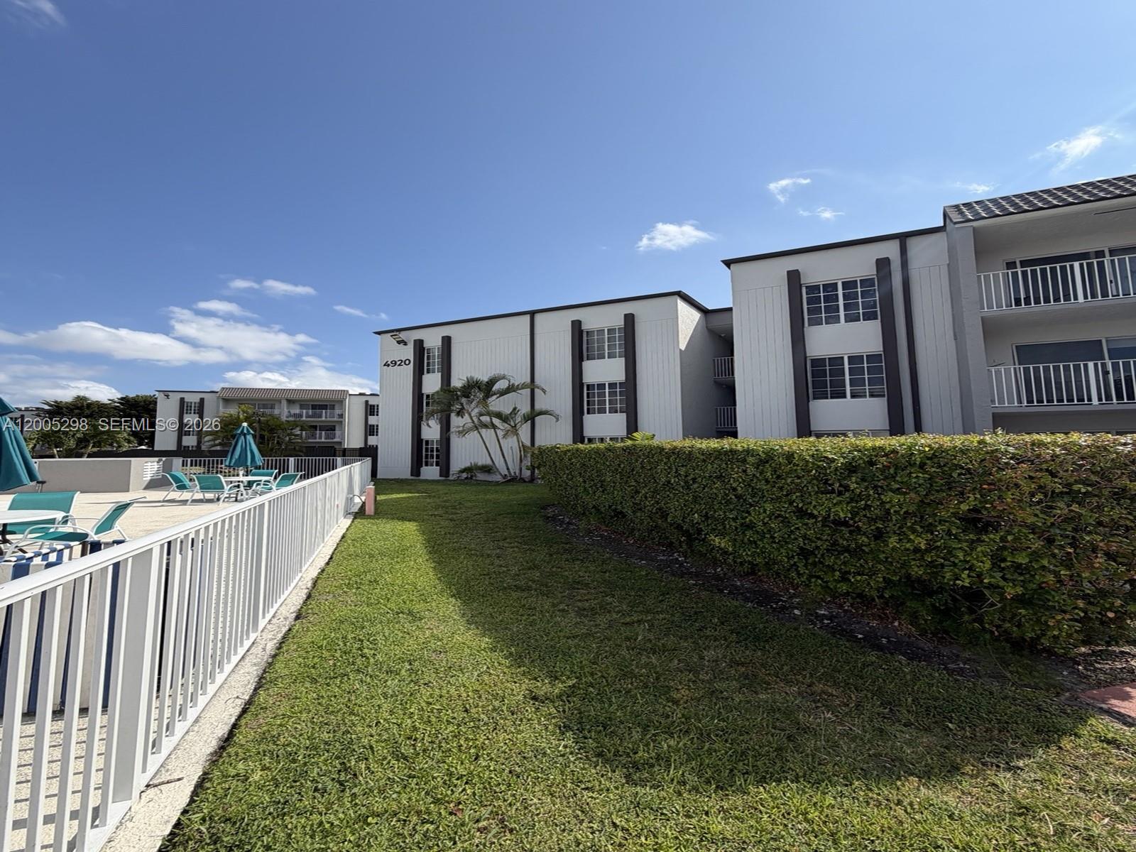A multi-story apartment building stands next to a swimming pool area with lounge chairs — 4920 NW 79th Ave # 313, Doral FL 33166, DORAL, FL