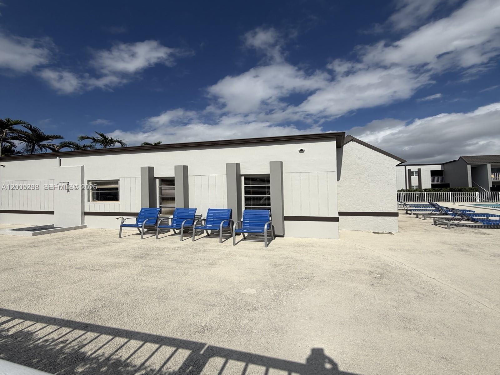 A white building exterior features four blue chairs on a concrete pool deck — 4920 NW 79th Ave # 313, Doral FL 33166, DORAL, FL