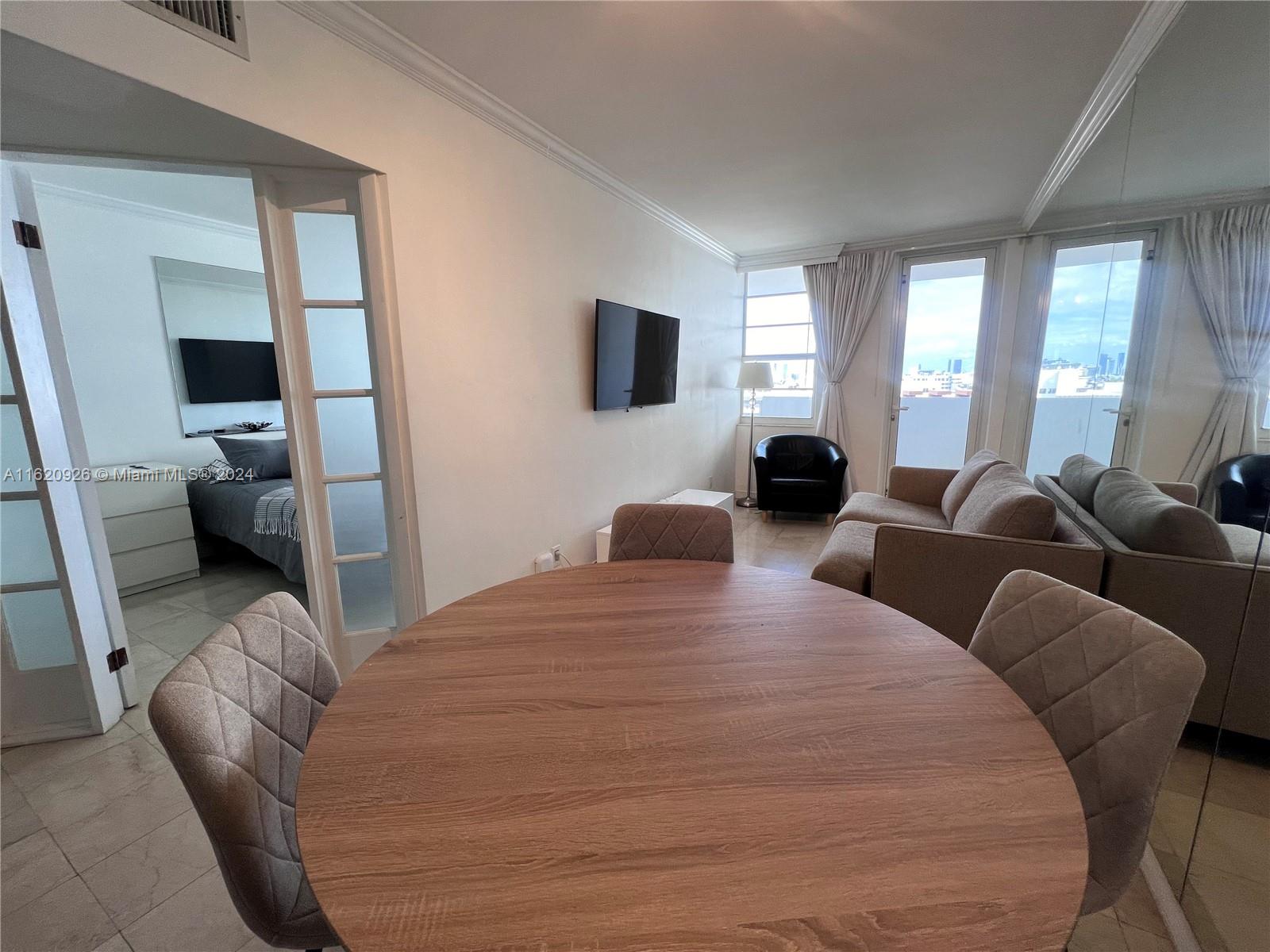 A dining area with a round wooden table opens into a living room with balcony access — 100 Lincoln Rd # 820, Miami Beach FL 33139, MIAMI BEACH, FL