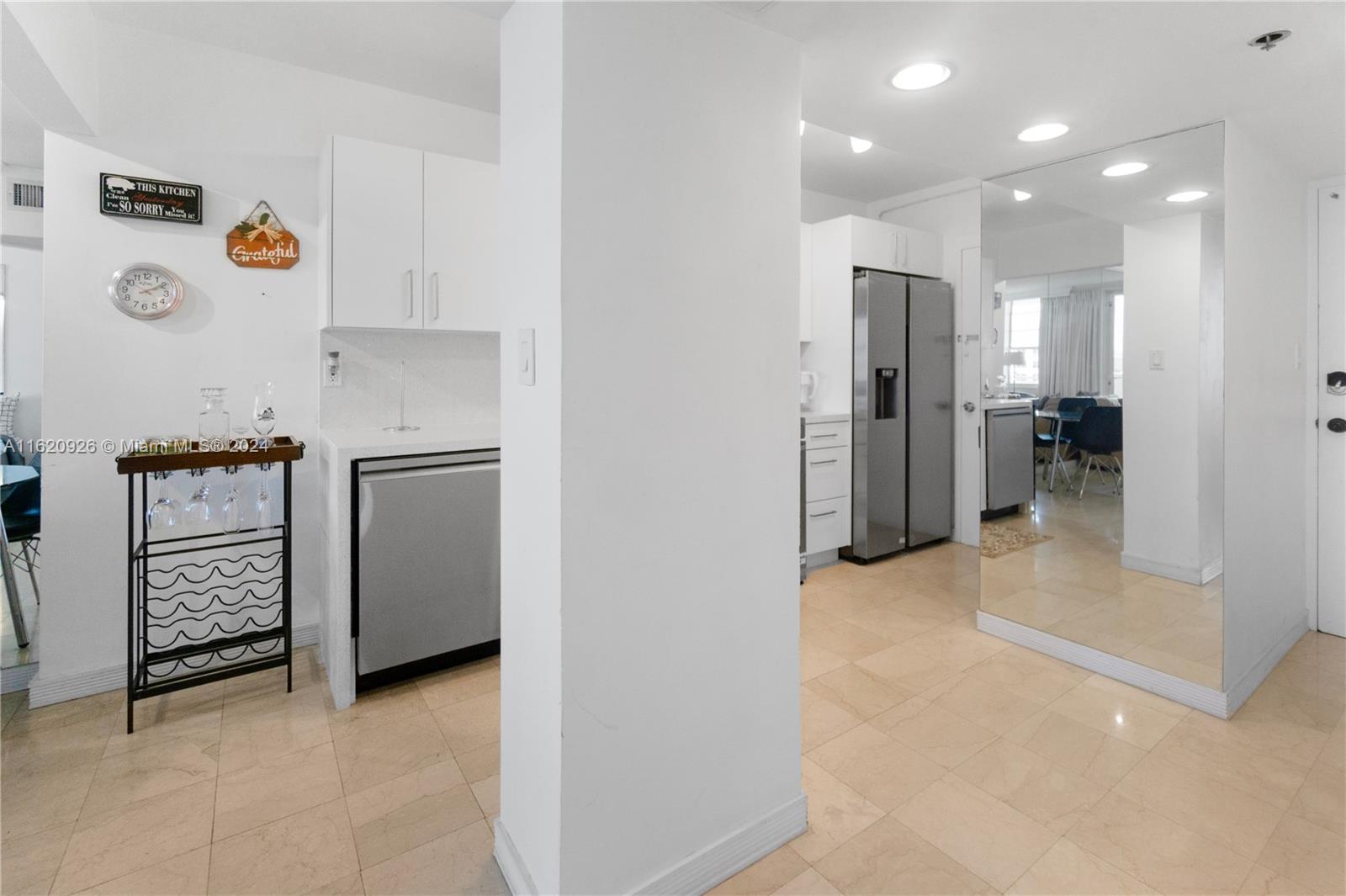 A kitchen features white cabinets, stainless steel appliances, and a mirrored wall in the dining area — 100 Lincoln Rd # 820, Miami Beach FL 33139, MIAMI BEACH, FL