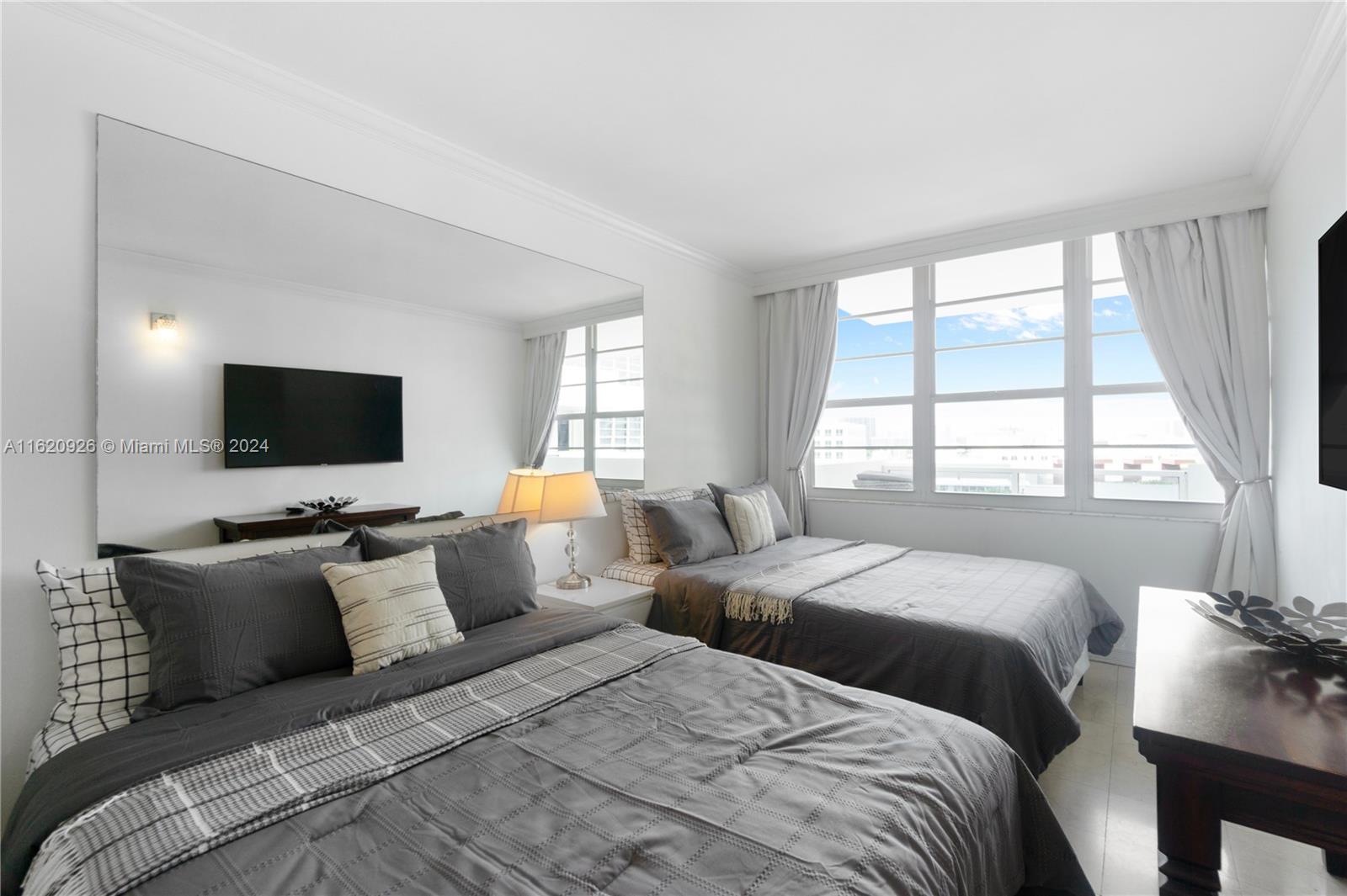 A bedroom features two beds, a large wall mirror, and windows with white curtains — 100 Lincoln Rd # 820, Miami Beach FL 33139, MIAMI BEACH, FL