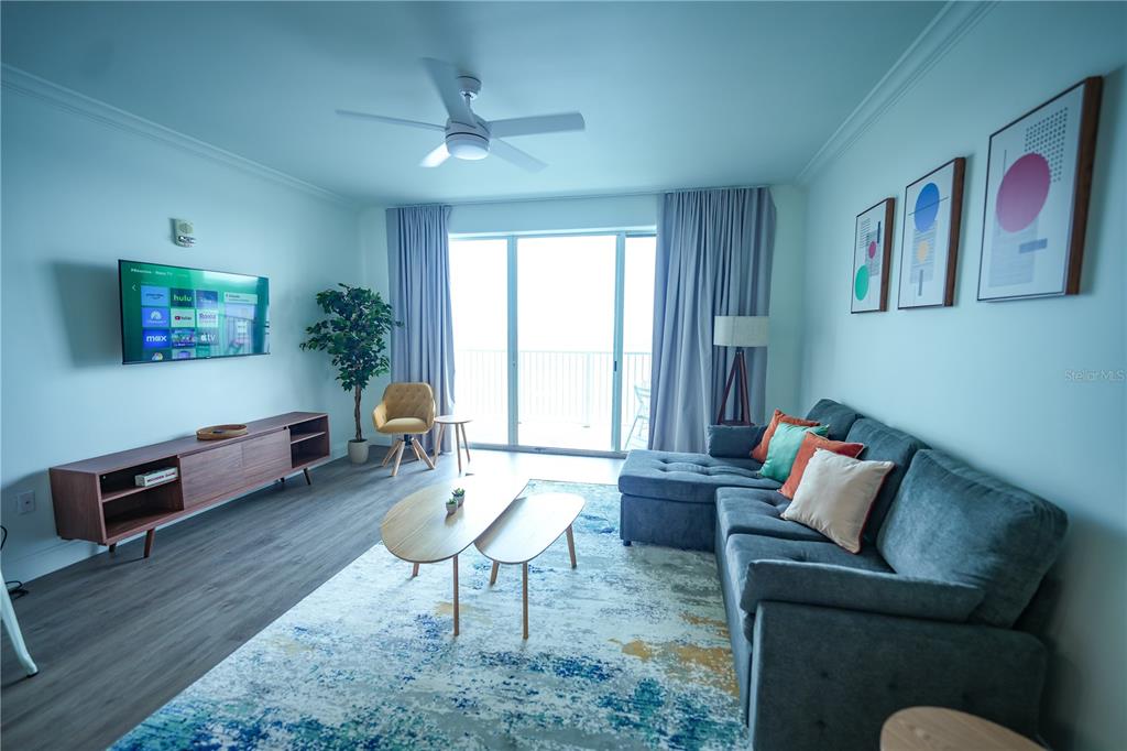 A living room features a blue sectional sofa, a wooden media console, and a balcony — 13415 BLUE HERON BEACH DRIVE UNIT 1108, ORLANDO, FL