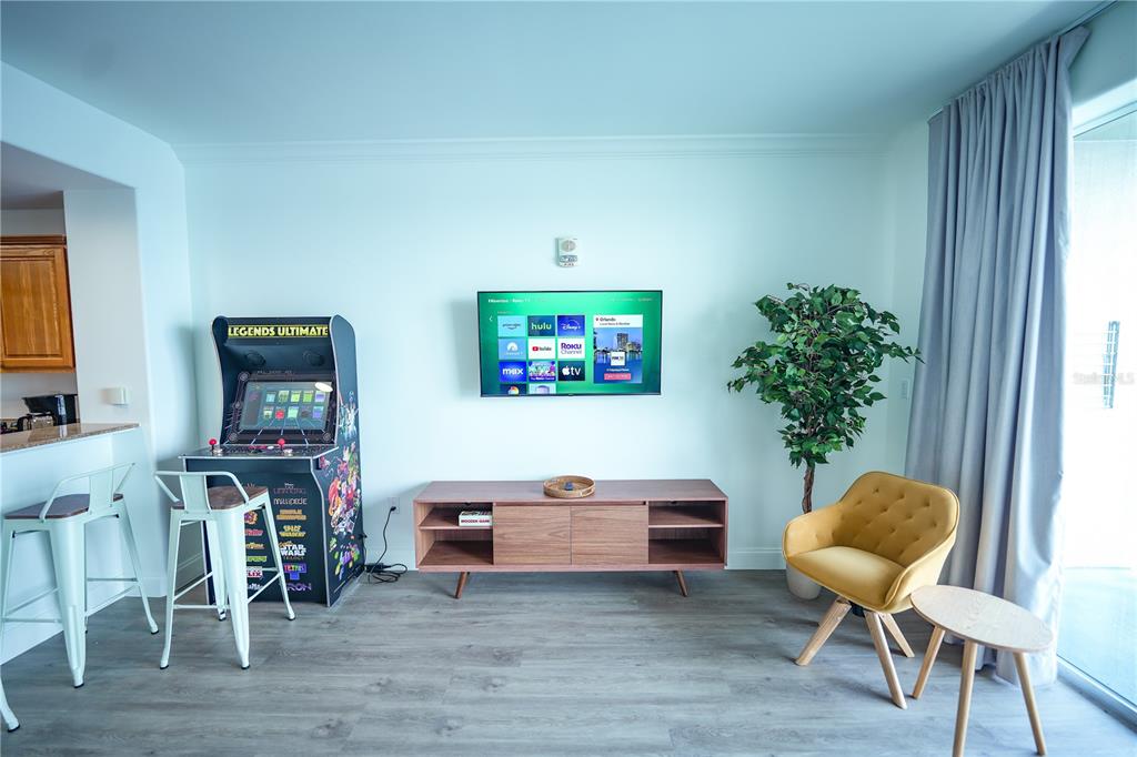 A living room features a wall-mounted television, a wooden media console, and an arcade cabinet — 13415 BLUE HERON BEACH DRIVE UNIT 1108, ORLANDO, FL