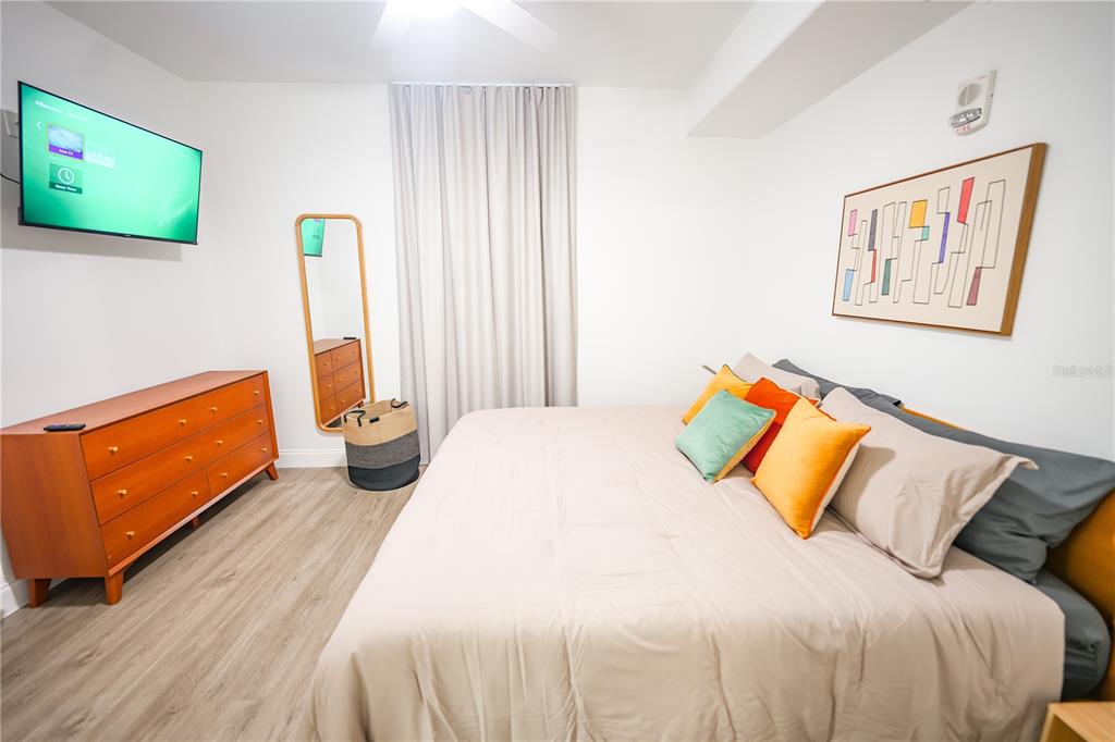 A bedroom features a bed with colorful pillows, a wooden dresser, and a wall-mounted television — 13415 BLUE HERON BEACH DRIVE UNIT 1108, ORLANDO, FL