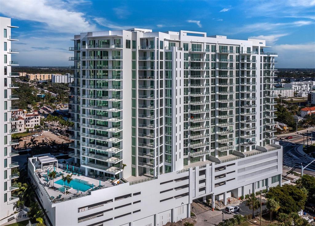An aerial view of a tall, modern white apartment building with balconies and a pool deck — 301 QUAY COMMONS UNIT 1003, SARASOTA, FL