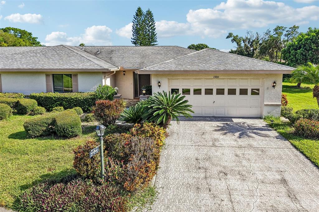 A single-story house with a gray shingled roof, white stucco walls, and a two-car garage — 1304 LELAND DRIVE, SUN CITY CENTER, FL