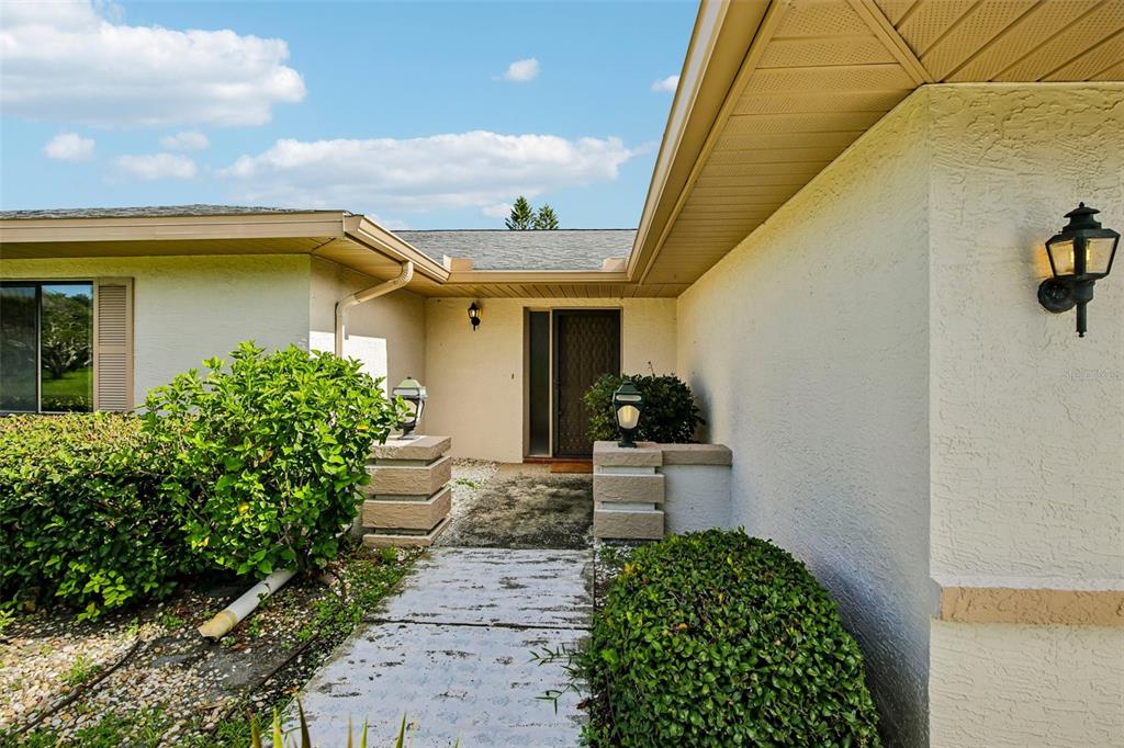 A concrete walkway leads to the front entrance of a house with light-colored stucco walls — 1304 LELAND DRIVE, SUN CITY CENTER, FL