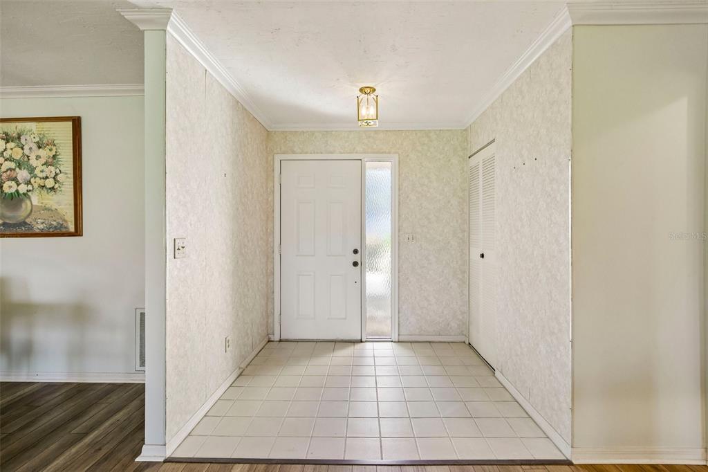 A foyer with white tile flooring, wallpapered walls, a white front door, and a closet — 1304 LELAND DRIVE, SUN CITY CENTER, FL