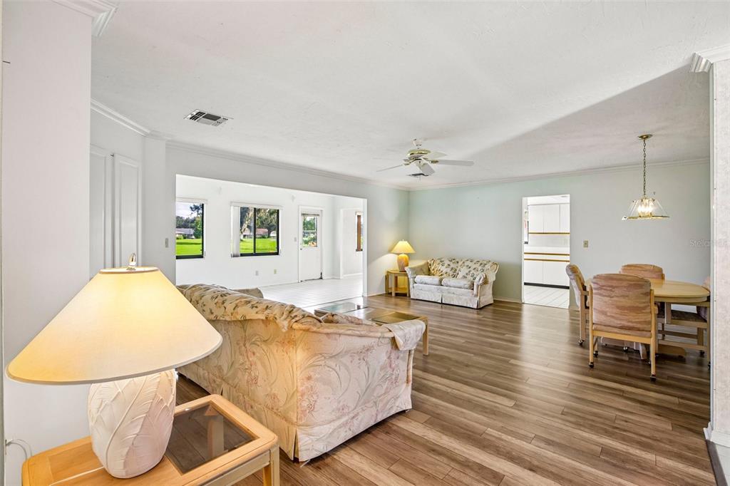 A spacious living and dining area features light wood-look flooring and floral-patterned furniture — 1304 LELAND DRIVE, SUN CITY CENTER, FL