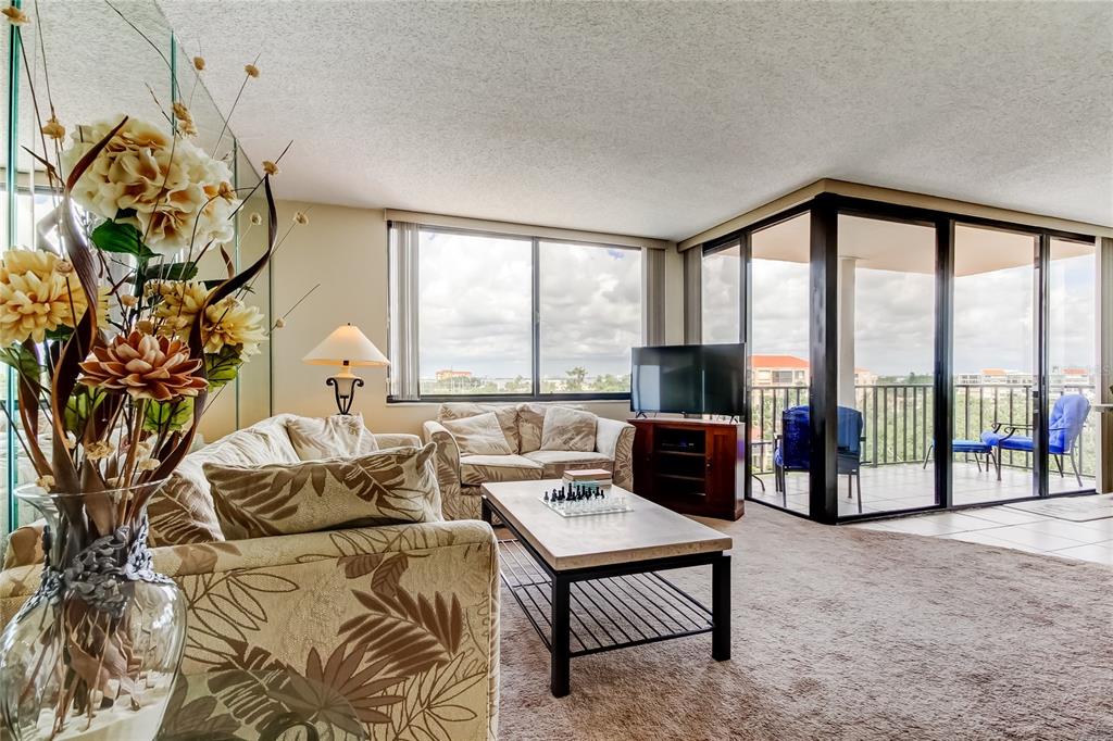 A living room with patterned sofas, a coffee table, and a balcony with outdoor seating — 6218 PALMA DEL MAR BOULEVARD S UNIT 606, ST PETERSBURG, FL
