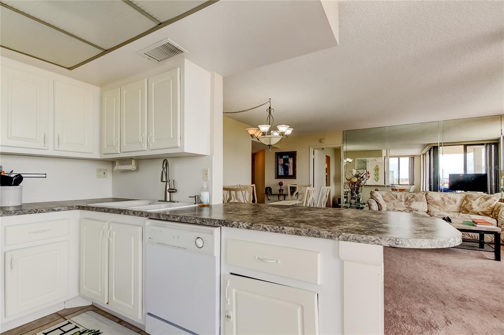 A kitchen with white cabinets and a stone-look countertop overlooks a carpeted living area — 6218 PALMA DEL MAR BOULEVARD S UNIT 606, ST PETERSBURG, FL