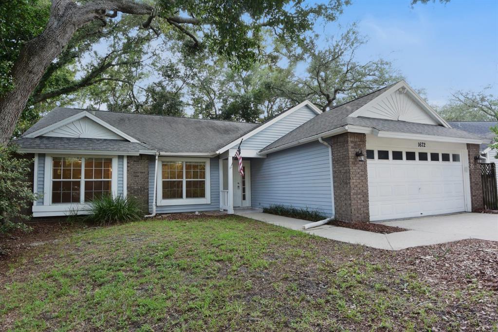 A single-story house with blue siding, a brick-front garage, and a large tree in front — 1672 COUNTRYWOOD STREET, TARPON SPRINGS, FL