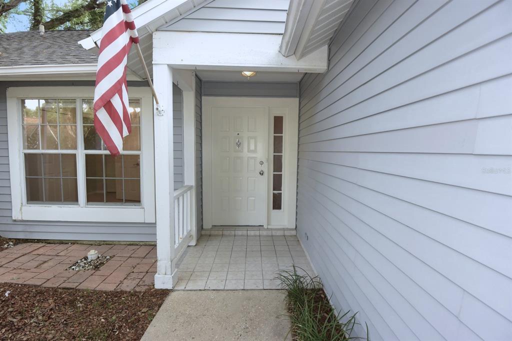 The front entrance features a white door with sidelights, light blue siding, and an American flag — 1672 COUNTRYWOOD STREET, TARPON SPRINGS, FL