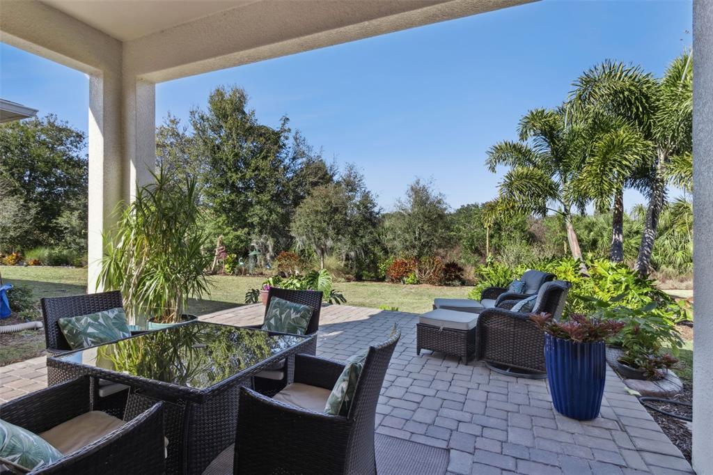 A covered patio features wicker furniture on a paver floor overlooking a grassy backyard — 7637 SAND PIERRE COURT, KISSIMMEE, FL
