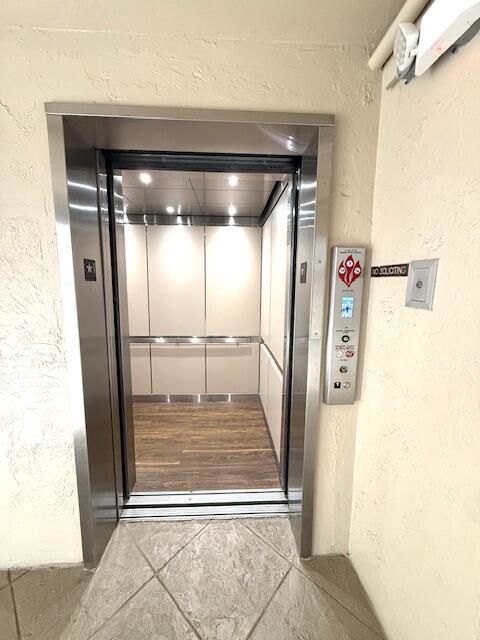 An open elevator with stainless steel doors and wood-look flooring in a beige hallway — 4 Royal Palm Way # 601, Boca Raton FL 33432, BOCA RATON, FL
