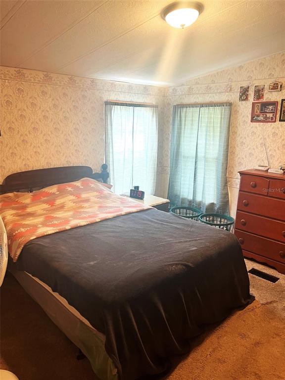 A bedroom features a bed with a patterned blanket, floral wallpaper, and a wooden dresser — 4538 OAK STREET, FRUITLAND PARK, FL