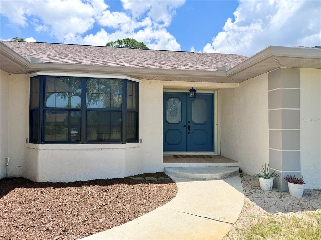 A beige house exterior features a blue double front door and a large bay window — 1087 BAY HARBOR DRIVE, ENGLEWOOD, FL