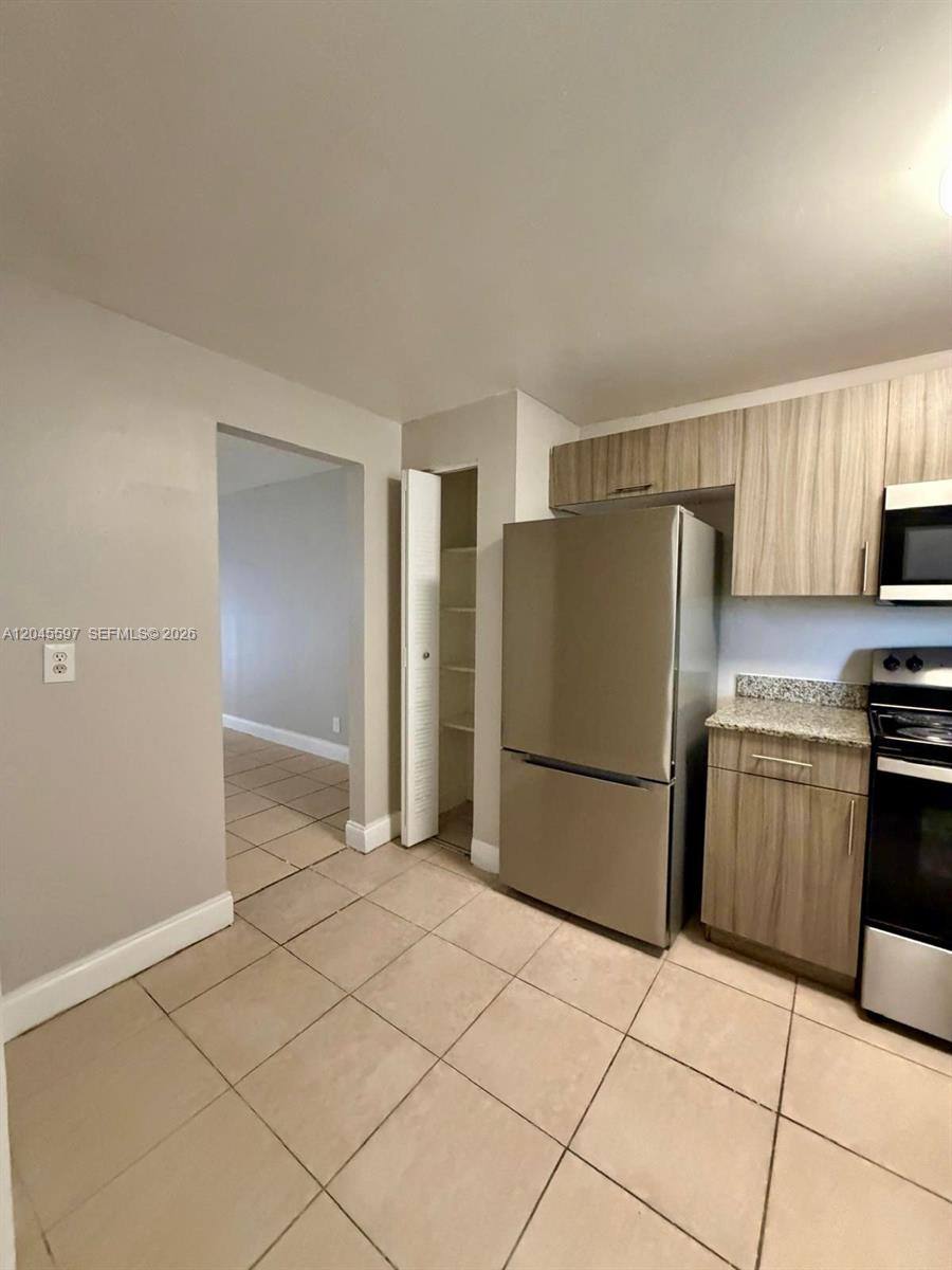 A kitchen features light wood cabinets, stainless steel appliances, and beige tile flooring — 2111 NW 55th Ave # 211, Lauderhill FL 33313, LAUDERHILL, FL