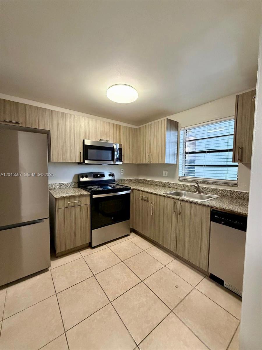 A kitchen features light wood-grain cabinets, stainless steel appliances, and beige tile flooring — 2111 NW 55th Ave # 211, Lauderhill FL 33313, LAUDERHILL, FL