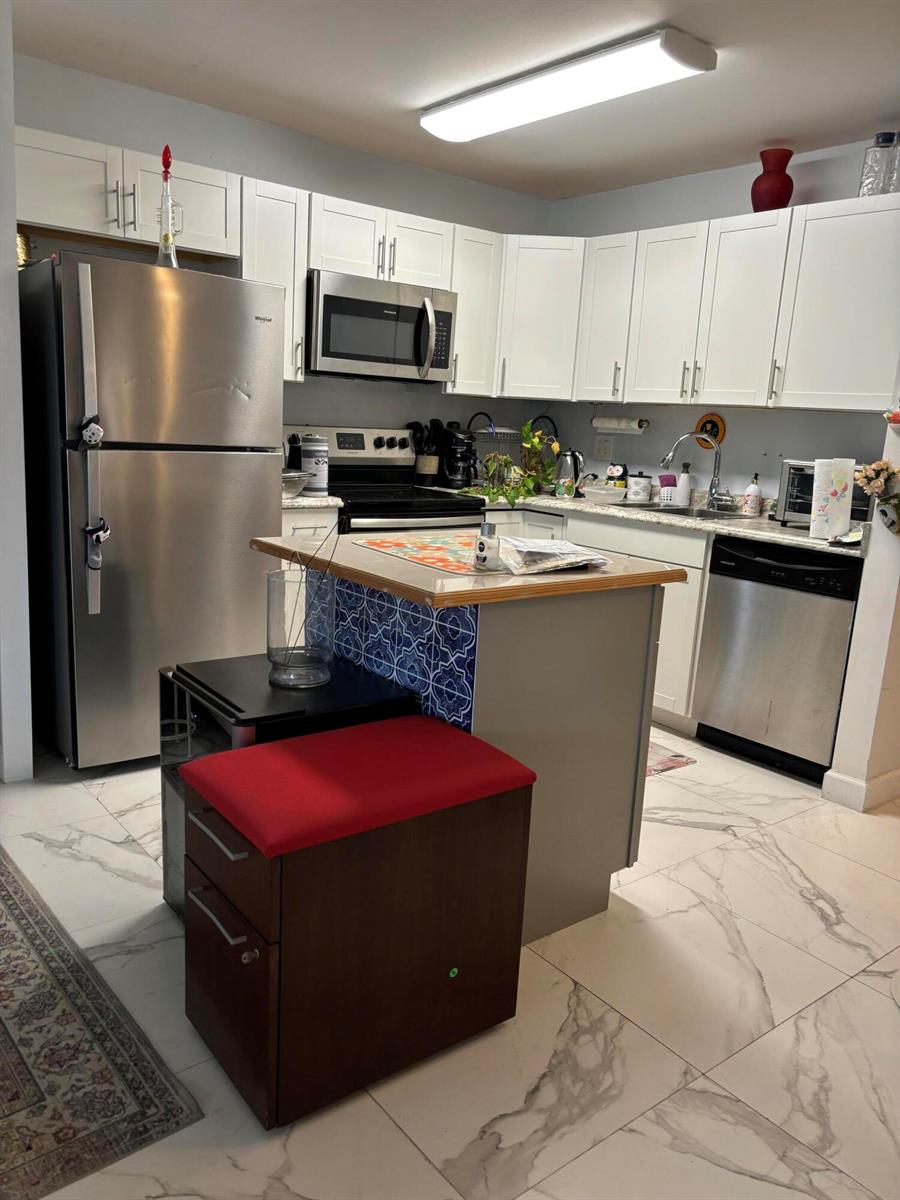 A kitchen features white cabinetry, stainless steel appliances, a tiled island, and marble-patterned floor tiles — 325 Andover, West Palm Beach FL 33417, WEST PALM BEACH, FL