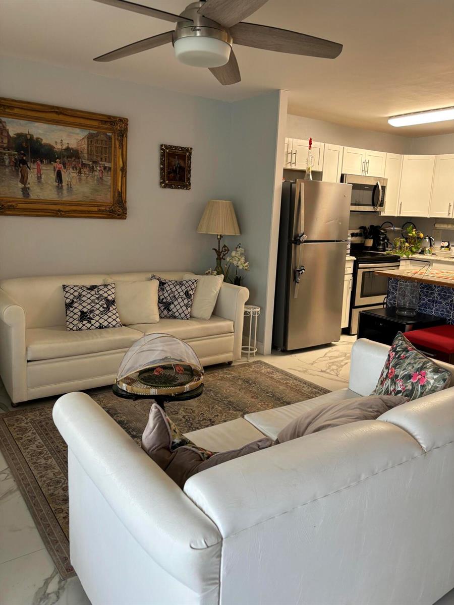 A living room with white sofas and a rug opens into a kitchen with stainless appliances — 325 Andover, West Palm Beach FL 33417, WEST PALM BEACH, FL