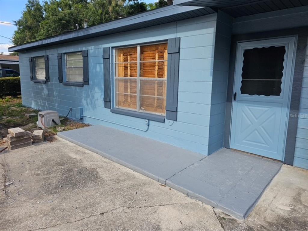 A blue exterior wall features a front door, a large window with shutters, and concrete steps — 10209 LOLA STREET, TAMPA, FL