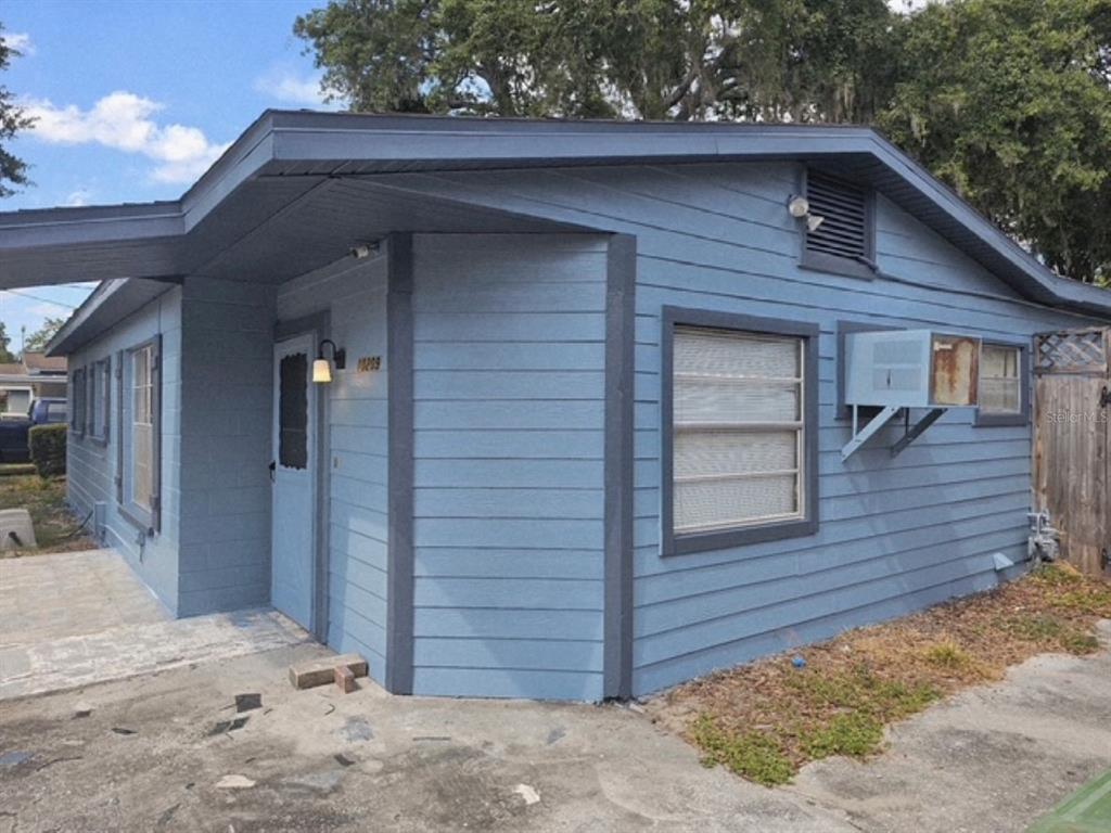 A blue house exterior with horizontal siding, a window air conditioning unit, and a carport — 10209 LOLA STREET, TAMPA, FL