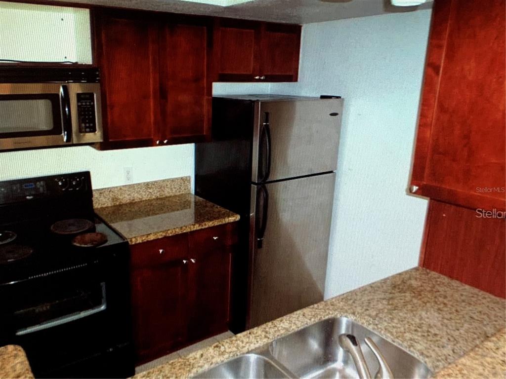 A kitchen features dark wood cabinets, granite countertops, and stainless steel appliances — 5124 CONROY ROAD UNIT 635, ORLANDO, FL