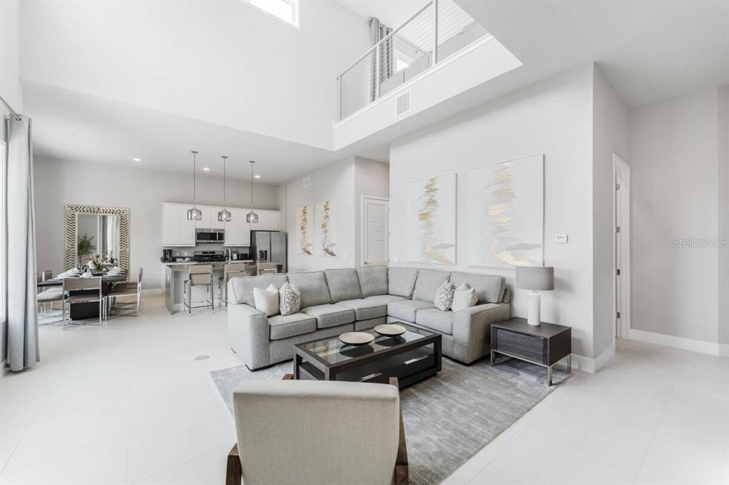 A bright, open-concept living room and kitchen area with high ceilings and neutral modern decor — 7760 SANDY RIDGE DRIVE UNIT 226, REUNION, FL