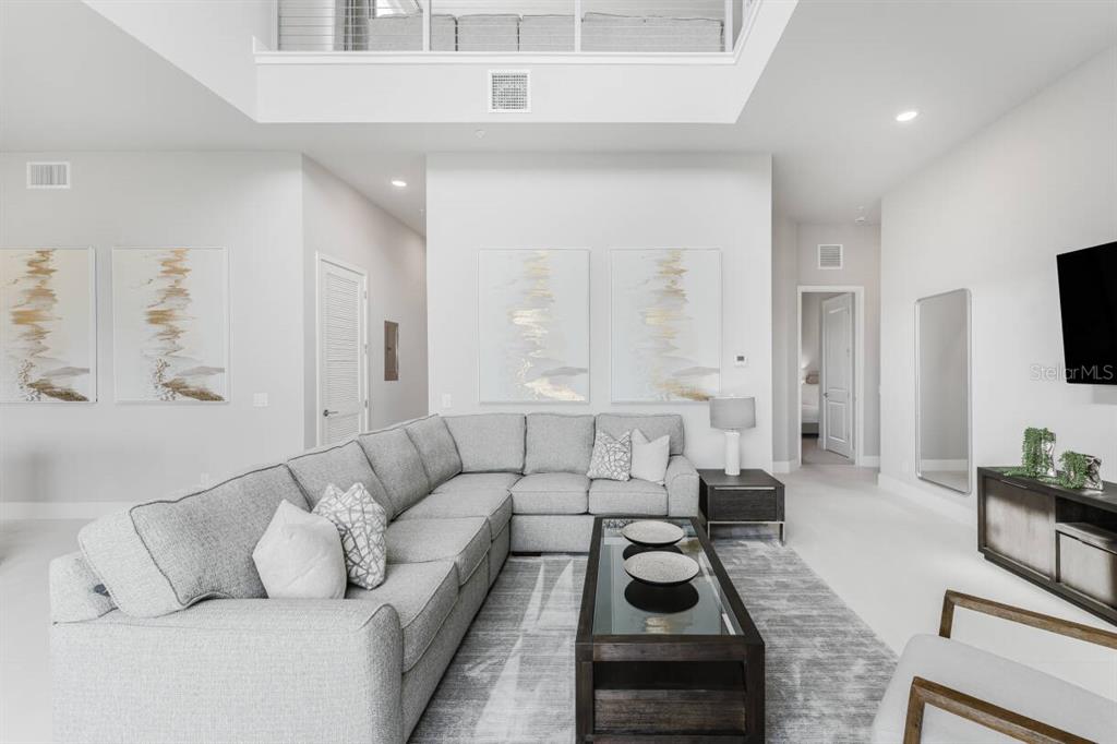 A modern living room features a large gray sectional sofa, a glass-topped coffee table, and artwork — 7760 SANDY RIDGE DRIVE UNIT 226, REUNION, FL