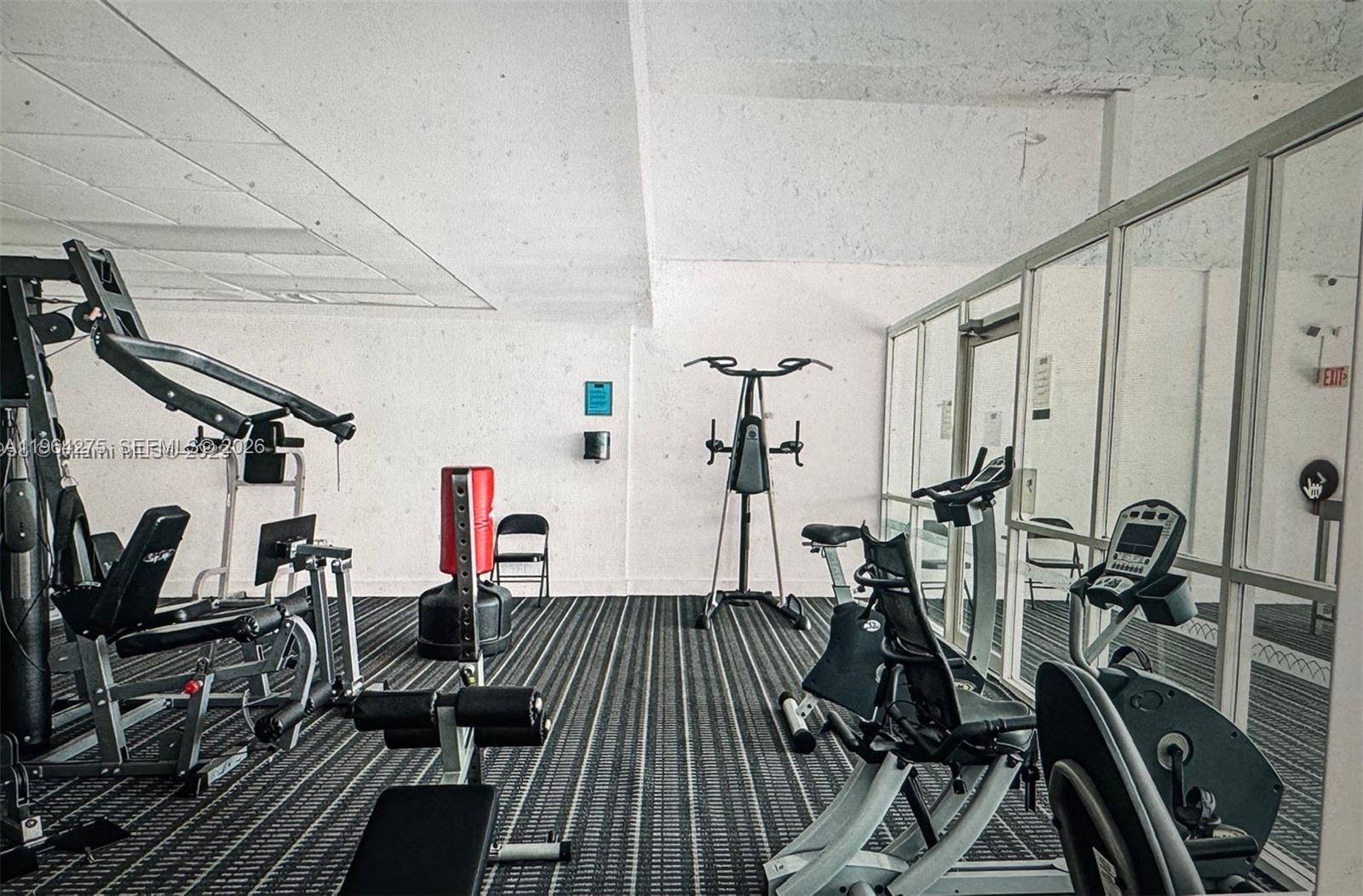 A gym room features various exercise machines, a punching bag, and striped carpeting — 496 NW 165th St Rd # 614, Miami FL 33169, MIAMI, FL