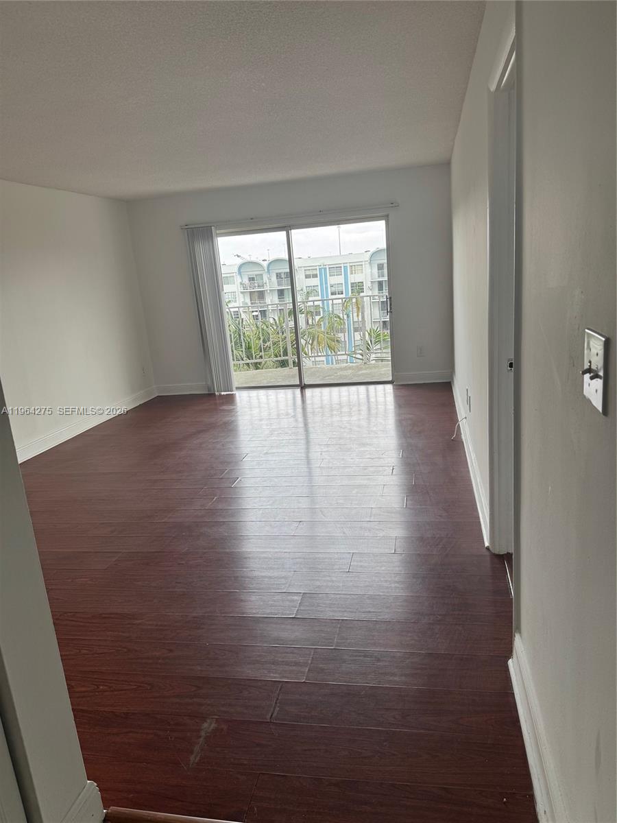 An empty room features dark wood-look flooring, white walls, and a sliding glass balcony door — 496 NW 165th St Rd # 614, Miami FL 33169, MIAMI, FL