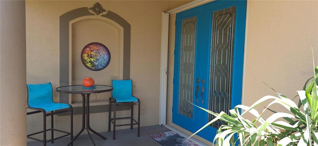 A covered porch features a bistro set, a decorative wall niche, and bright blue double doors — 19 MEDALIST WAY, ROTONDA WEST, FL