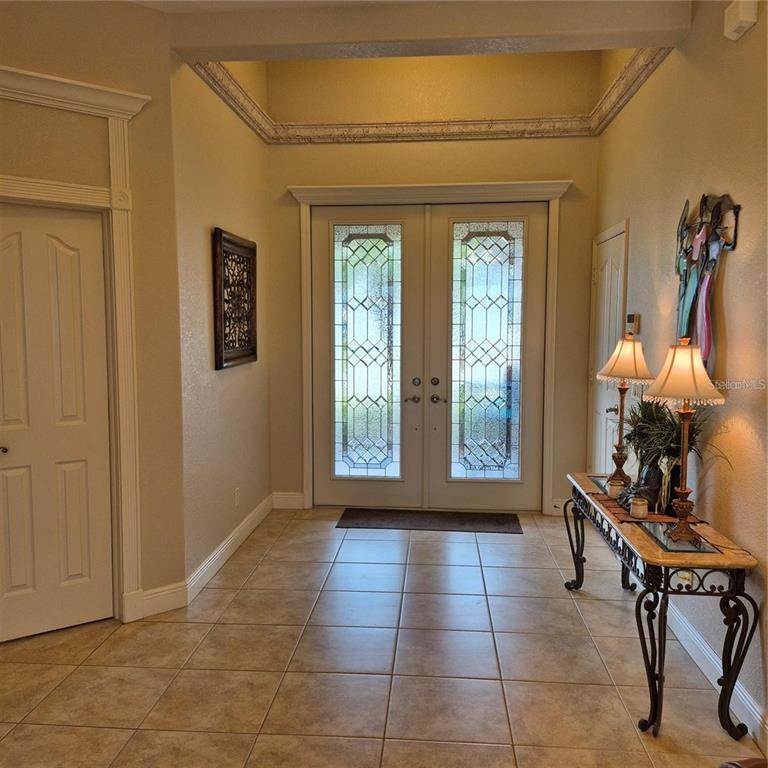 A tiled entryway features double glass-paneled front doors, a console table, and decorative crown molding — 19 MEDALIST WAY, ROTONDA WEST, FL